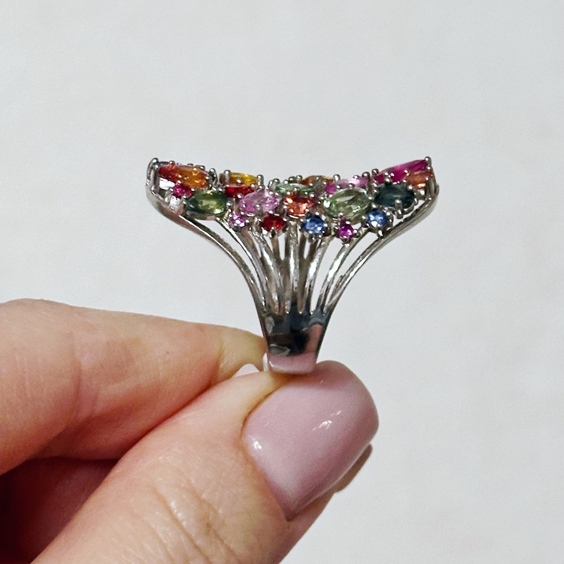 Multicolored gemstone ring held by a hand against a white background